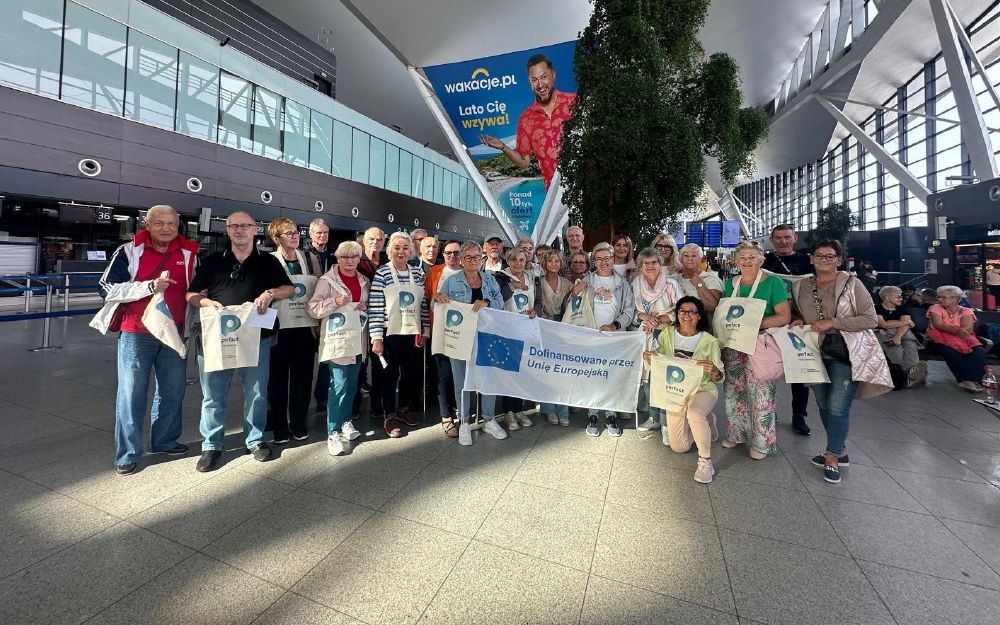 Grupa słuchaczy fundacji z torbami Perfact i flagą Unii Europejskiej na lotnisku w Gdańsku, przed wyjazdem na mobilność Erasmus+